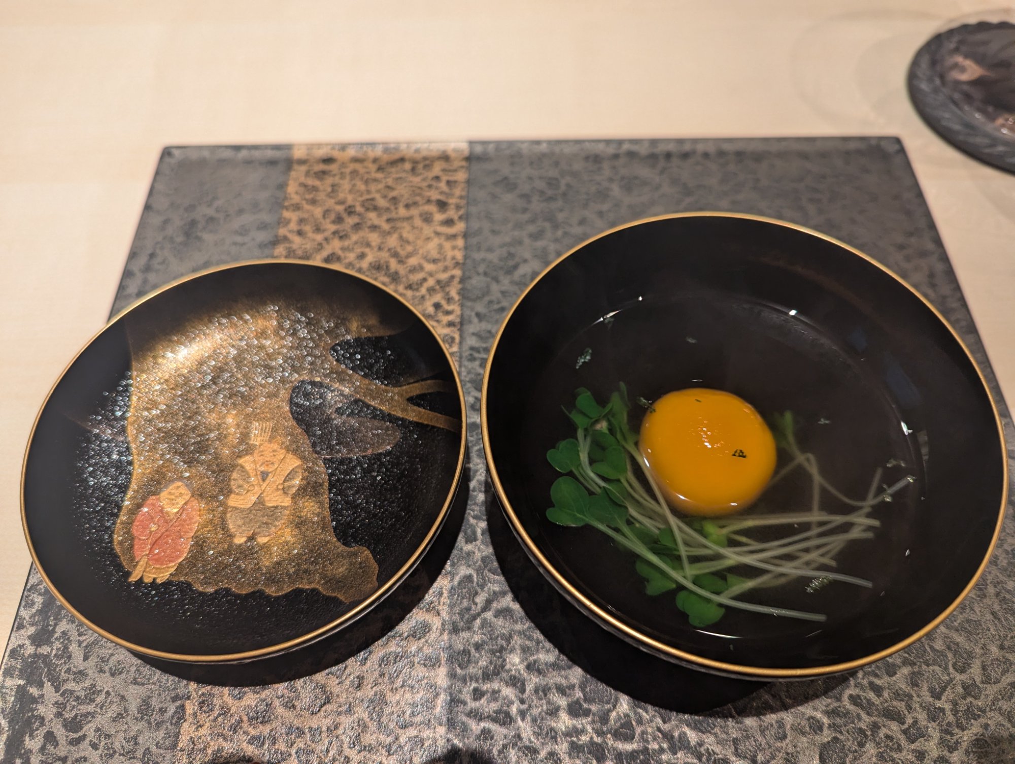 Sakizuke. A deep egg yolk and green shoots against black lacquerware with gold maki-e on the lid