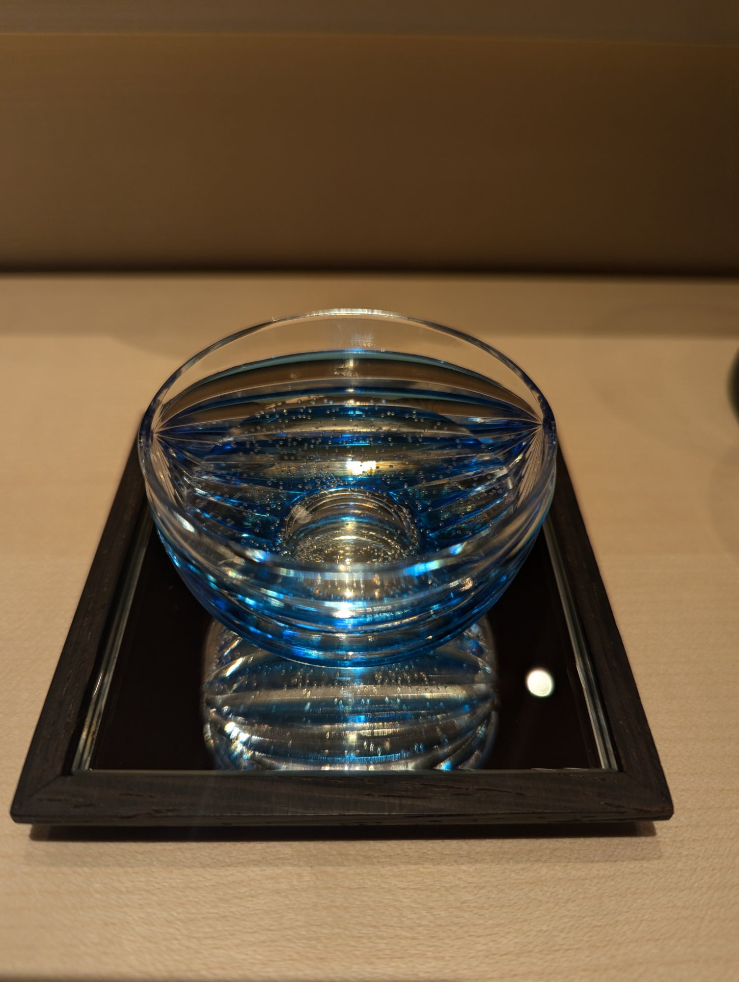 A Horiguchi kiriko cut-glass sake cup in cobalt blue, placed on a black tray and catching the light through its stripe pattern