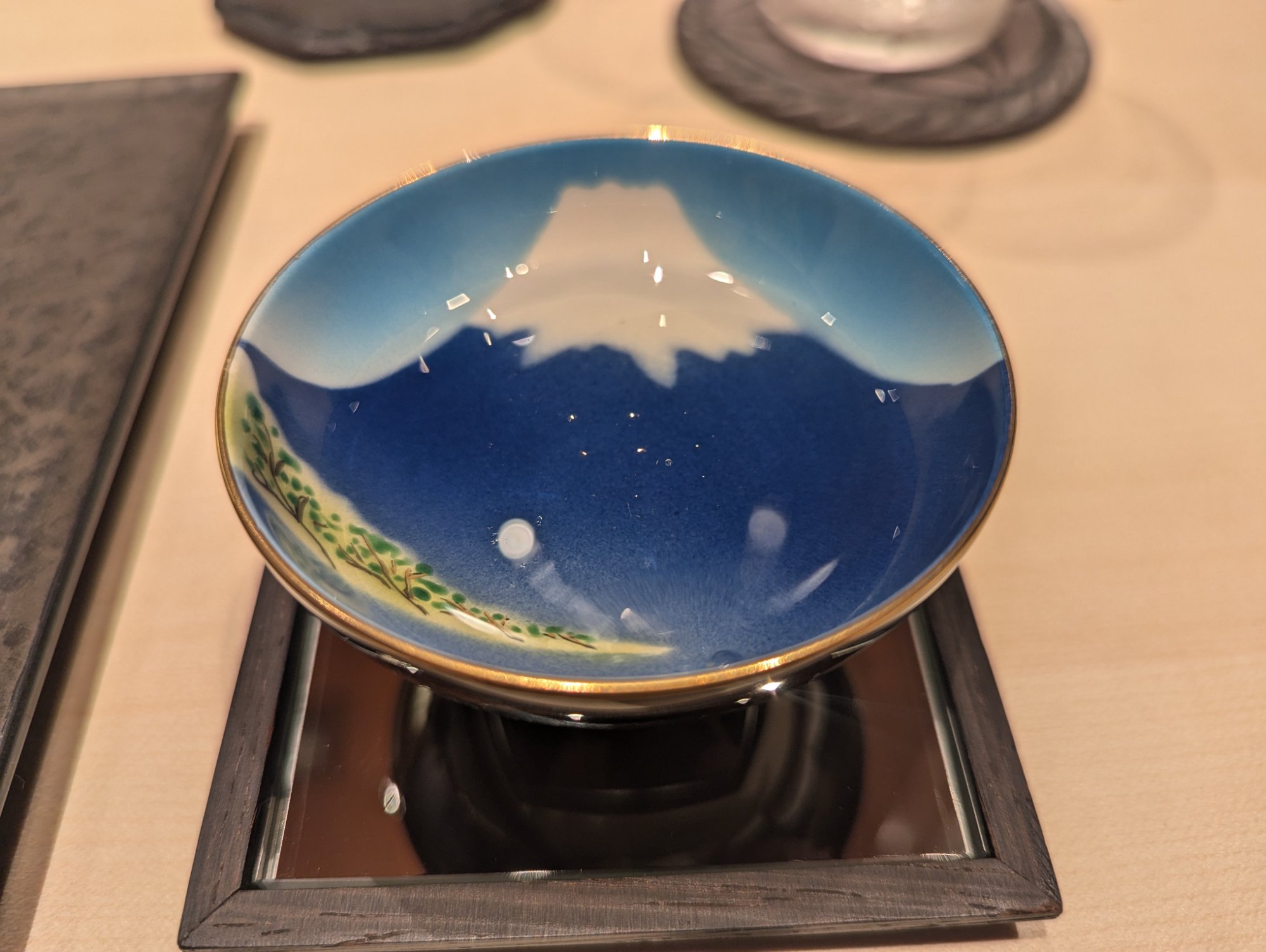 A sake cup painted with Mount Fuji on the interior, the detailed artwork visible through the glass