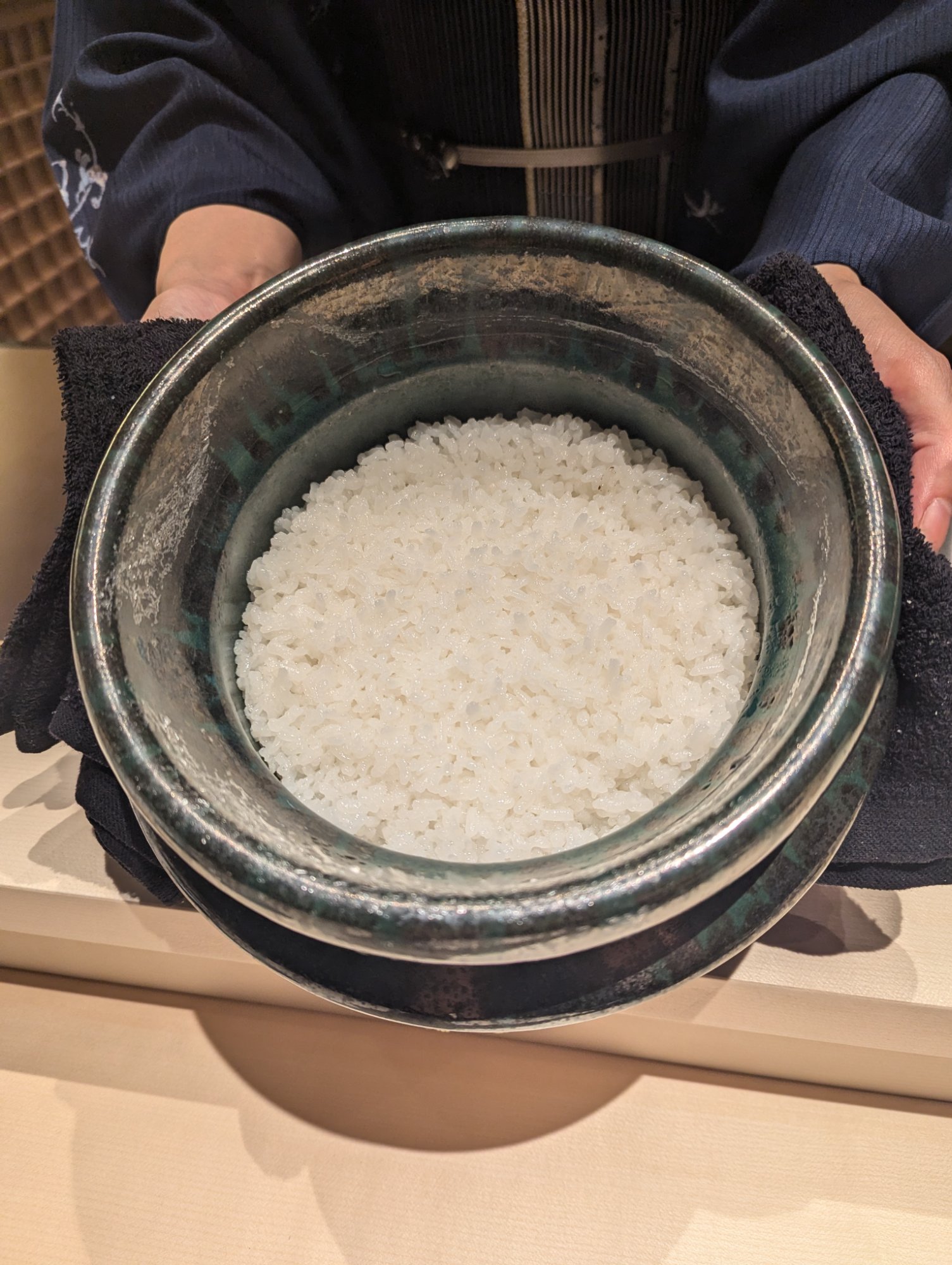 The okami carrying the rice pot with both hands, the lustrous cooked rice visible inside